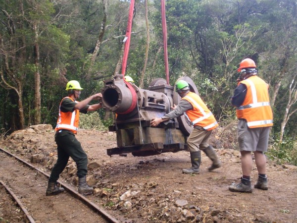 DOC staff manouvere part of the historic compressor into place beside the tramway